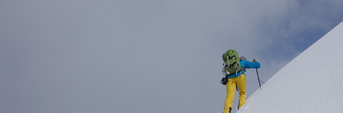 Eine Person mit Ski im steilen Aufstieg zum Flaschenpeak.