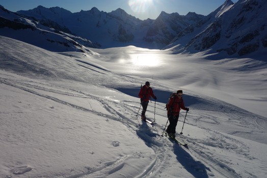 Zwei Skitourengaenger im Licht der Morgensonne steigen einen Schneehang hoch.