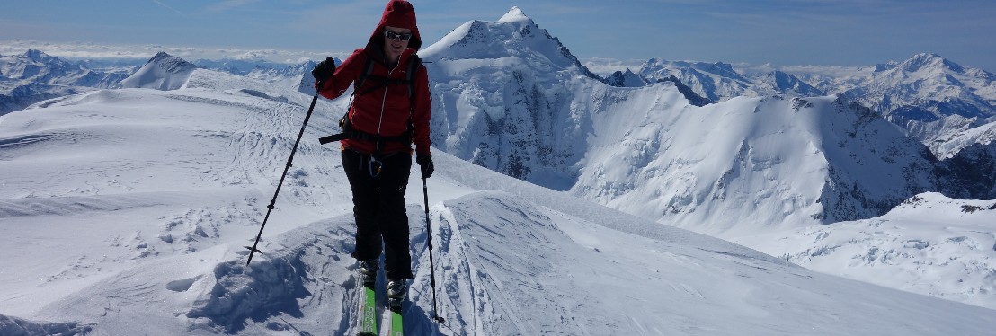 Eine Frau mit roter Jacke, erreicht mit den Ski den Gipfel der Aebniflue