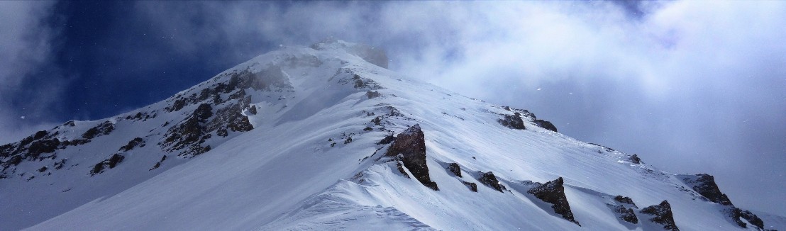 Skitouren-Lawinengrundausbildung Wind verfrachtet Schnee über einen Berggipfel