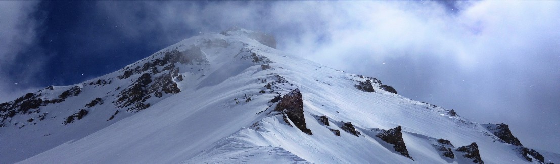 Wind verfrachtet Schnee über einen Berggipfel