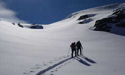 Zwei Skitourenfahren ziehen ihre Aufstiegsspur im unberührtem Schnee.