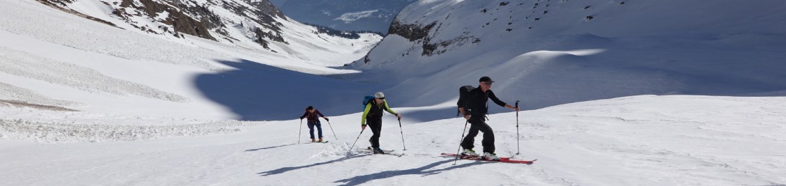 Drei Skitourenpersonen im Aufstieg in einem Tal