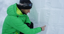 Ein Teilnehmer in grüner Jacke und Mütze prüft ein Schneeprofil